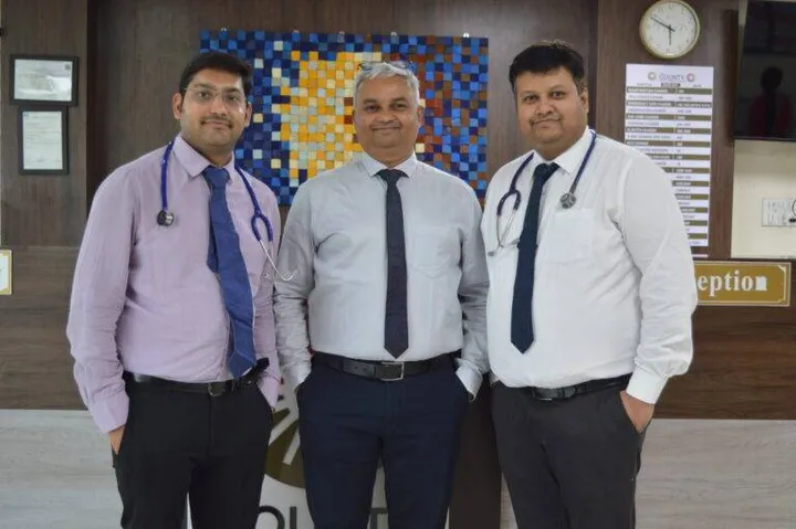 Three doctors photographed in the reception area beneath the hospital tariff board