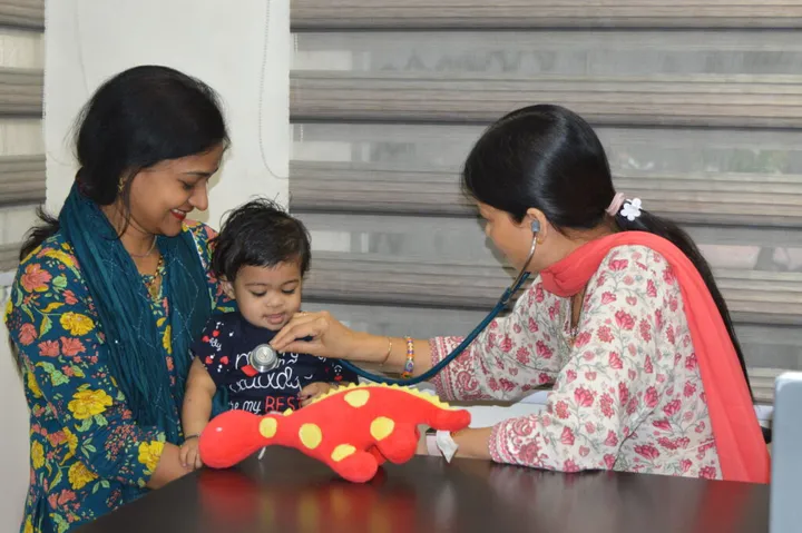 A paediatrician listening to a baby’s chest with a stethoscope while the mother holds him on her lap