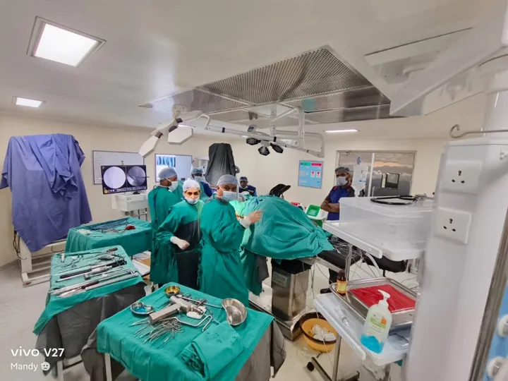An orthopaedic procedure under way, with C-arm images displayed on the theatre monitor and instrument trays laid out in the foreground