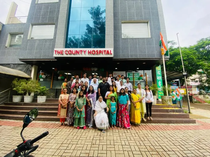 A wider view of the staff group photograph outside the hospital entrance, with the national flag flying beside the building