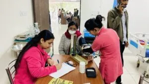 Nurses registering patients at a desk during a health camp, with a queue forming in the corridor behind