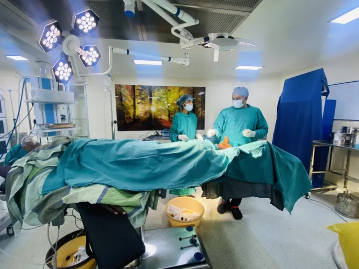Two gowned surgeons at the operating table under the LED shadowless theatre lights