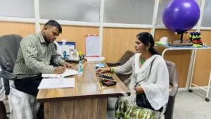 A doctor writing a prescription for a patient seated across the consulting desk at a camp
