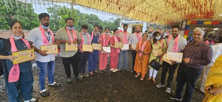 The outreach team lined up under a decorated marquee at a community event, each holding a certificate