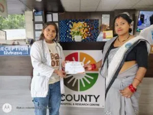 A doctor presenting a certificate to a patient in front of The County Hospital logo backdrop