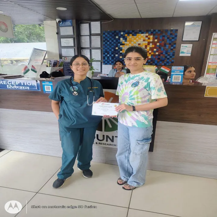 A doctor in scrubs handing a young woman her participation certificate at the reception desk during the vaccination drive