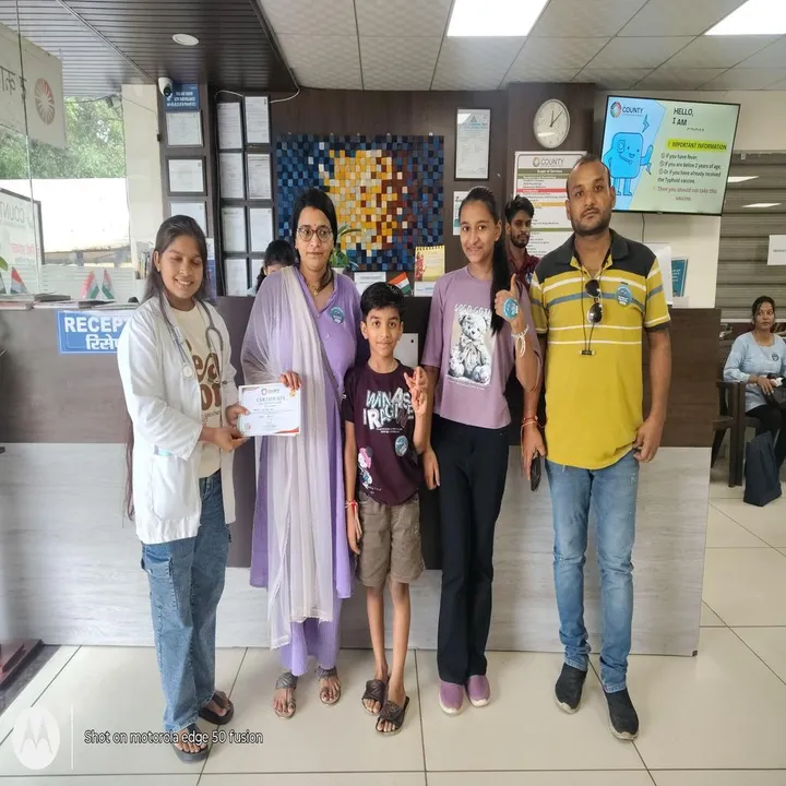 A family standing with a doctor at reception after the vaccination drive, holding their certificate