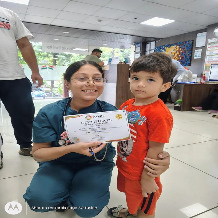 A doctor kneeling beside a small boy to show him the certificate of participation from the vaccination drive