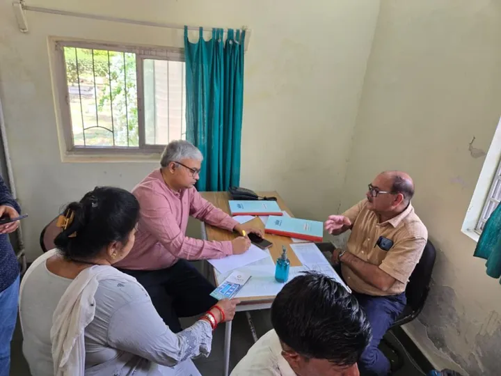 Doctors running a consultation table at a village outreach camp, with patients seated across from them