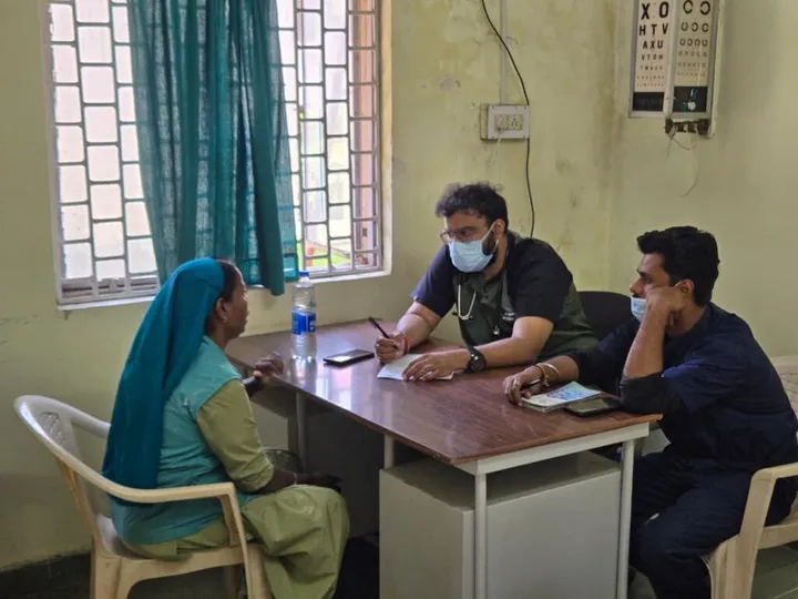A doctor taking a woman’s history at an outreach camp, with an eye test chart on the wall behind